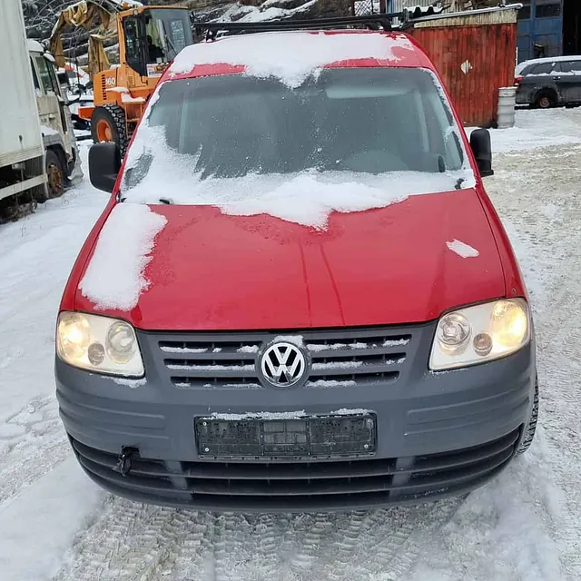 Rød Volkswagen varebil med snø på panser parkert på isete underlag ved verksted.