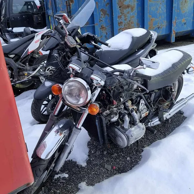 Motorsykkel med synlig motor og snø på setet parkert ved container på opphuggeri.