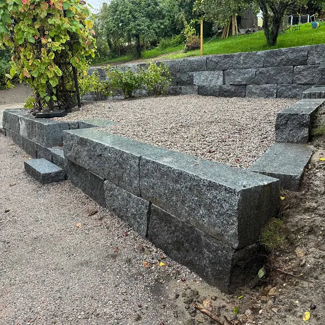 Opparbeidet uteområde med granittmur, trapper og gruslagt platå i hage.