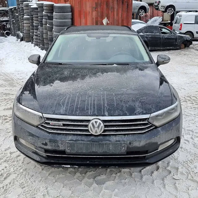 Sort Volkswagen med skitt og snø parkert foran container og dekk på bilopphuggeri.